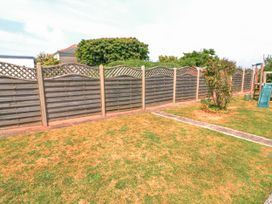 A backyard with a wooden lattice fence a patchy lawn a small bush and a children's slide at Joymead in Malborough