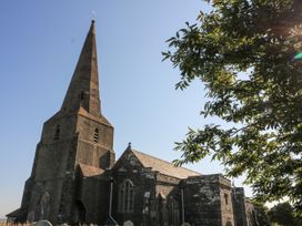 An old stone church with a tall spire and arched windows next to a tree with green leaves