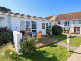 A patio with a round table and four chairs outside a white house with sliding glass doors and garden plants at Cape A9 Norton Near Freshwater