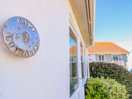 A white exterior wall with a round metal sign reading cape 9 cottages next to glass doors and bushes at Cape A9 Norton Near Freshwater
