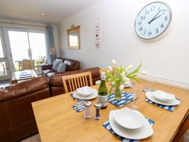 A dining table set with plates glasses a bottle and flowers next to a living area with leather sofas and a wall clock at Cape A9 Norton Near Freshwater