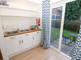 A kitchenette with two sinks a bread box and a fire extinguisher next to a sliding glass door with patterned curtains leading to a patio with a table and chair at Cape A9 Norton Near Freshwater