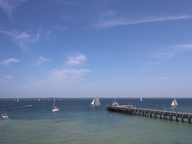 A view of a wooden pier extending into the sea with several sailboats and a clear sky at Cape A9 Norton Near Freshwater