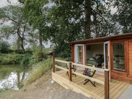 A wooden cabin with a deck near water at Carps Well Lodge Hatton near Shrewley