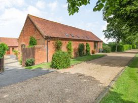 A brick building with a tiled roof surrounded by bushes and trees with a gravel driveway at Willow in Wood Norton near Foulsham