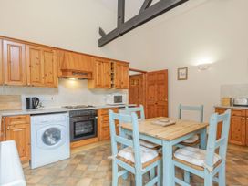 A kitchen with wooden cabinets a washing machine an oven a microwave a dining table with four chairs and a wooden door at Willow in Wood Norton near Foulsham
