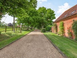A gravel driveway lined with trees next to a red brick building and wooden fence at Willow in Wood Norton near Foulsham