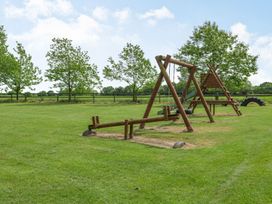 An outdoor playground with swings, a slide, and a seesaw on a grassy field at Willow in Wood Norton near Foulsham