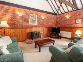 A living room with green sofas a wooden coffee table a TV on a stand and exposed brick walls at Pear Tree in Wood Norton