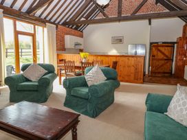 A living room with green armchairs a wooden coffee table dining table with chairs and a kitchen counter at Pear Tree in Wood Norton