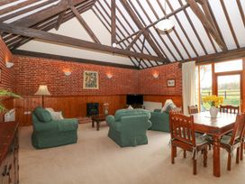 A living room with green armchairs a wooden dining table and exposed wooden beams at Pear Tree in Wood Norton