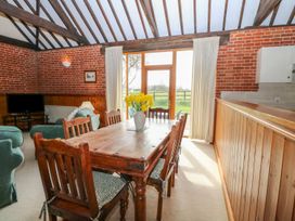 A dining area with a wooden table and chairs and a living room with green armchairs at Pear Tree in Wood Norton
