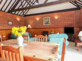 A dining table with yellow flowers in a vase and wooden chairs in a room with exposed brick walls and wooden beams at Pear Tree in Wood Norton