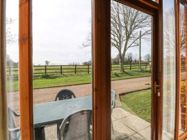 View through glass doors showing an outdoor patio with a plastic table and chairs a gravel driveway grass a fence and trees at Pear Tree in Wood Norton