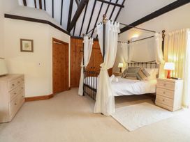 A bedroom with a four-poster bed with white curtains two bedside tables with lamps and a chest of drawers at Pear Tree in Wood Norton