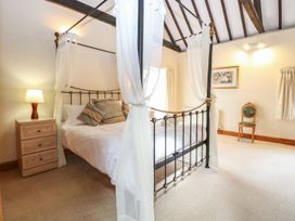 A bedroom with a four poster bed a nightstand with a lamp a chair and a framed picture at Pear Tree in Wood Norton