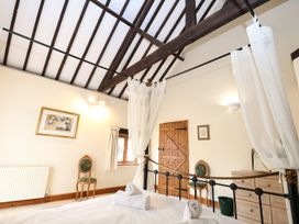 A bedroom with a canopy bed two green chairs a wooden door and a chest of drawers at Pear Tree in Wood Norton