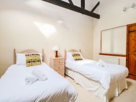 A bedroom with two single beds with white linens and patterned pillows a bedside table with a lamp and wooden door at Pear Tree in Wood Norton