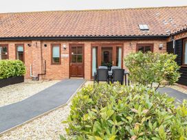 A brick building with a tiled roof a paved path plastic chairs and table and bushes in front at Holly Berry Wood Norton near Foulsham