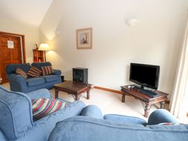 A living room with blue sofas a wooden coffee table a television on a wooden stand and a lamp at Holly Berry in Wood Norton near Foulsham