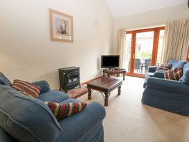 A living room with two blue sofas a small black stove a wooden coffee table and a TV near glass doors at Holly Berry Wood Norton near Foulsham