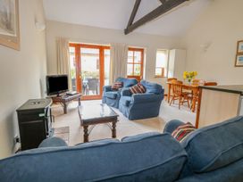A living room with blue sofas a wooden coffee table a television wood stove and a dining area with wooden chairs and table at Holly Berry Wood Norton near Foulsham