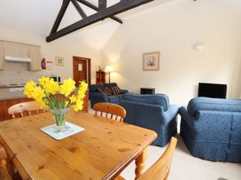 A living room with blue sofas a wooden dining table with yellow flowers and a kitchen area at Holly Berry Wood Norton near Foulsham