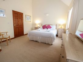 A bedroom with a double bed white linens pink pillows bedside tables lamps a wooden door chair and a dresser with a mirror at Holly Berry Wood Norton near Foulsham