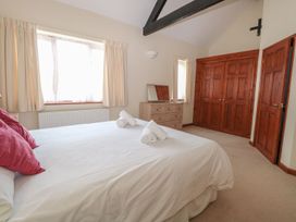 A bedroom with a large bed with white bedding and red pillows two rolled towels a wooden dresser with mirror wooden wardrobes and beige curtains at Holly Berry Wood Norton near Foulsham