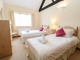 A bedroom with two single beds with white bedding and pink cushions a wooden dresser and chair and a bedside table with a lamp at Holly Berry Wood Norton near Foulsham