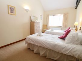 A bedroom with two single beds with white linens and red pillows a wooden chest of drawers a chair and a window with curtains at Holly Berry Wood Norton near Foulsham