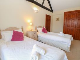 A bedroom with two single beds with white bedding and pink pillows a bedside table with a lamp a wooden wardrobe and a door at Holly Berry in Wood Norton near Foulsham