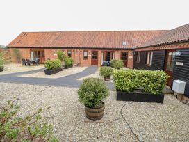 A courtyard with gravel and potted plants outside brick and black wooden buildings at Holly Berry Wood Norton near Foulsham