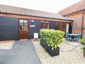 The exterior of a building with a dark door and windows a planter with green bushes and a patio table with chairs at Sycamore Wood Norton near Foulsham