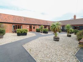 An outdoor courtyard with a tiled roof building surrounded by paved walkways and gravel areas with potted plants at Sycamore Wood Norton near Foulsham