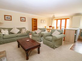 A living room with green sofas and armchairs with cushions a wooden coffee table a dining table with chairs and flowers near glass doors at Sycamore Wood Norton near Foulsham