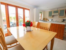 A dining table with chairs and a flower pot with red flowers in a kitchen with wooden cabinets and a sliding glass door at Sycamore in Wood Norton near Foulsham
