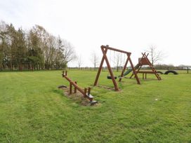 An outdoor play area with swings a slide a seesaw and large tires on grass at Sycamore in Wood Norton near Foulsham