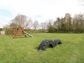 A playground with a wooden climbing frame slide and swings and two large tires in a grassy field at Sycamore in Wood Norton near Foulsham