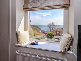 A window seat with two pillows and a bowl with a view of a garden hill and sea at 4 Bay View Terrace in Llandudno
