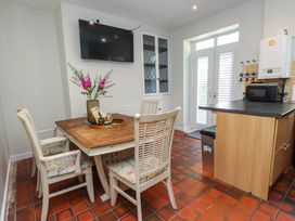 A kitchen dining area with wooden table and chairs a wall mounted television and double doors with shutters at 4 Bay View Terrace in Llandudno