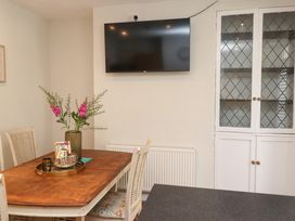 A dining area with a wooden table and chairs a vase with flowers a wall-mounted television and a glass-front cabinet at 4 Bay View Terrace in Llandudno