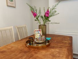 A wooden dining table with two white chairs and a tray holding a vase with flowers and a basket of packets at 4 Bay View Terrace in Llandudno