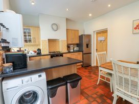 A kitchen with wooden cabinets a washing machine two trash bins a microwave and a dining table with chairs at 4 Bay View Terrace in Llandudno