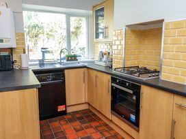 A kitchen with wooden cabinets black countertops a gas stove an oven a dishwasher a microwave a sink under a window and yellow tile backsplash at 4 Bay View Terrace in Llandudno
