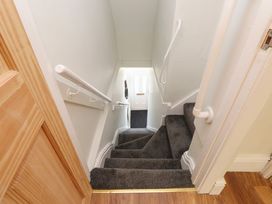 A staircase with grey carpet and white handrails leading to a white door at 4 Bay View Terrace in Llandudno