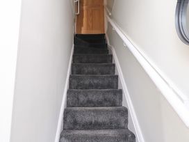 A narrow staircase with dark carpet and white walls at 4 Bay View Terrace in Llandudno