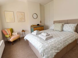 A bedroom with a bed with patterned bedding folded towels on the bed a wooden chest of drawers a round mirror an eclectic armchair two framed artworks and a small side table at 4 Bay View Terrace in Llandudno