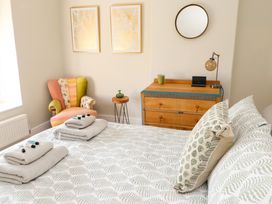 A bedroom with a bed covered in patterned bedding two folded towels on the bed a multicolored armchair a wooden dresser with a mirror and lamp on top at 4 Bay View Terrace in Llandudno