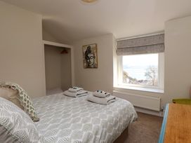 A bedroom with a bed having patterned bedding towels on the bed an open wardrobe a wall picture and a window with a view at 4 Bay View Terrace in Llandudno